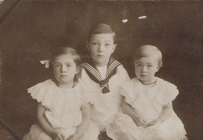 Kinderbild von Annelise links im Kleid neben ihren Geschwistern sitzend.