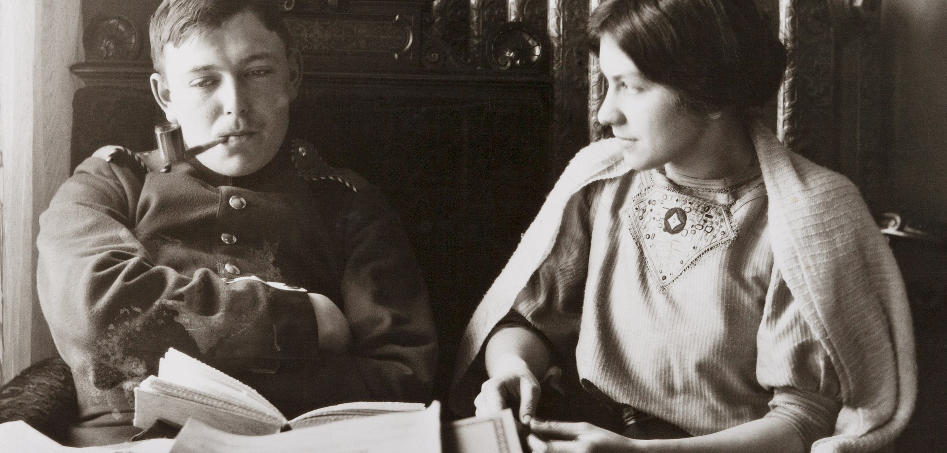 Das Paar August und Elisabeth Macke sitzt an einem Tisch, er raucht eine Pfeiffe, sie schaut ihn verliebt an.