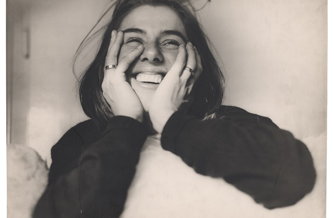 A smiling woman rests her head in her hands.