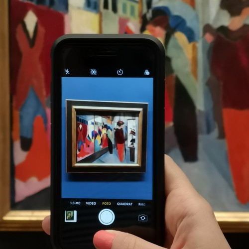 A woman takes a photo of a painting with her smartphone.
