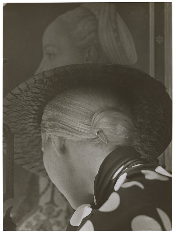 Hinterkopf einer Frau mit breitem Hut, im Hintergrund ein Gemälde