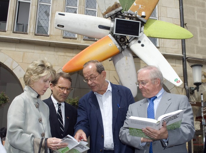 Das Foto zeigt Kasper König im Gespräch mit drei Personen. Im Hintergrund ist eine Skulptur zu sehen, die an ein buntes Windrad erinnert.