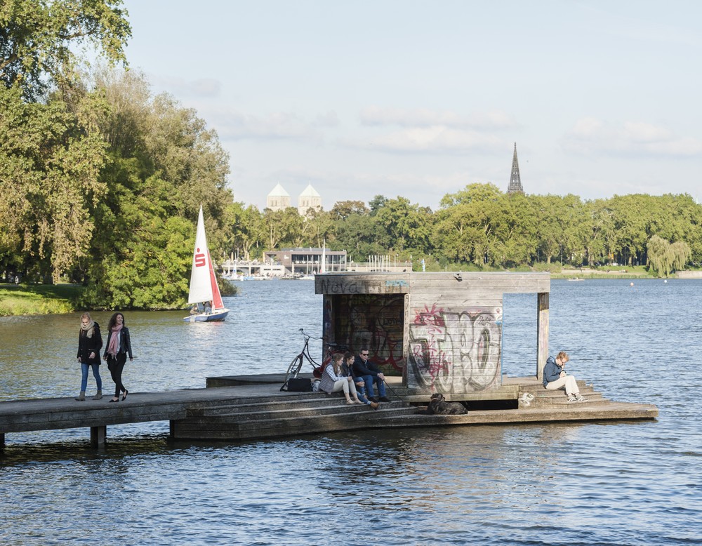 Das Foto zeigt ein Gewässer und einen Steg, der in das Wasser reicht. Auf dem Steg gibt es einen Pavillon.