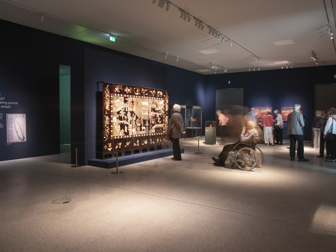 Das Bild zeigt eine Aufnahme aus der Ausstellung. Zu sehen ist ein blauer Raum mit einem großen Objekt, das aussieht, wie eine Wanddekoration. (vergrößerte Bildansicht wird geöffnet)