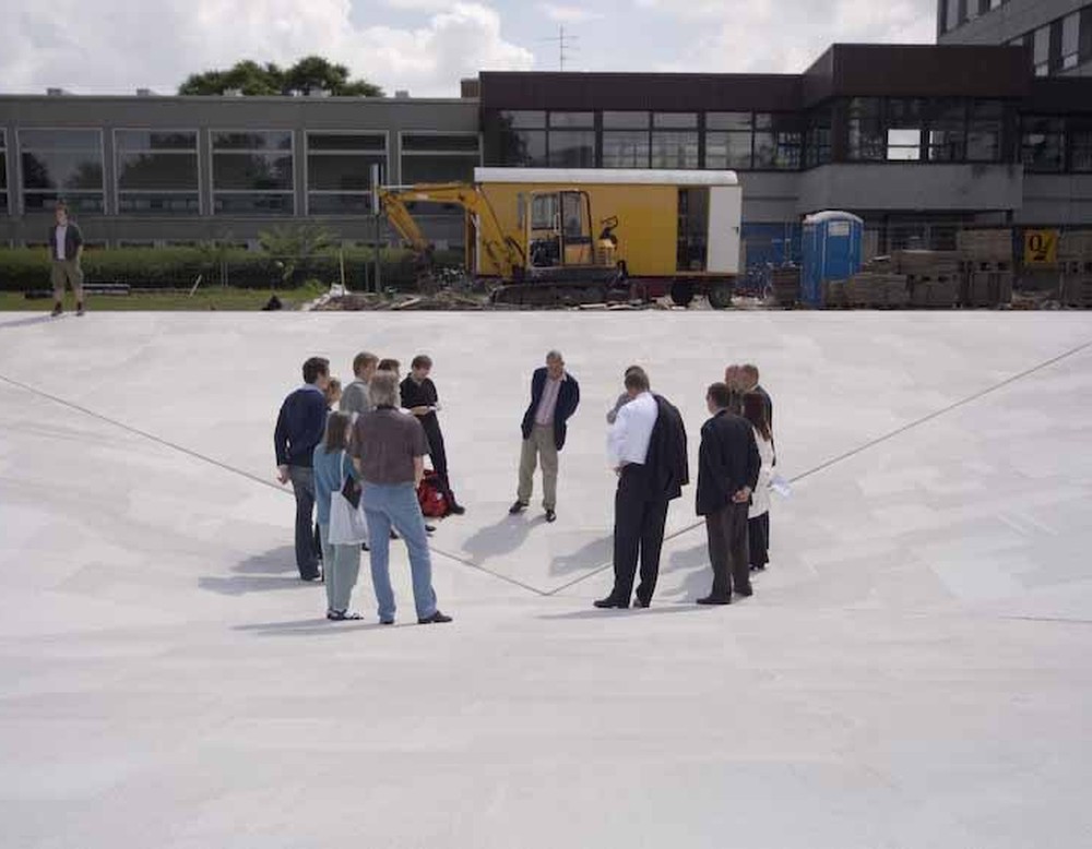 Das Bild zeigt mehrere Personen, die in einer abgesenkten, invertierten Pyramide stehen.
