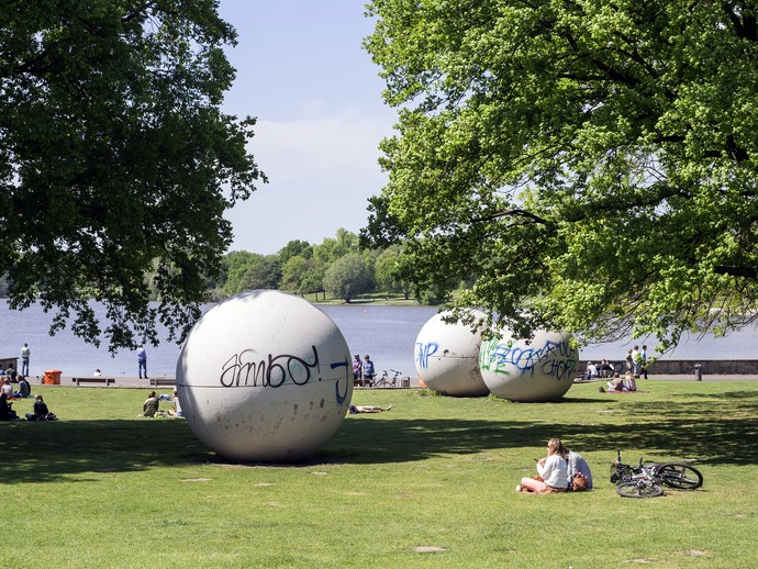 You see giant pool balls in a parc with trees and a lake in the background.