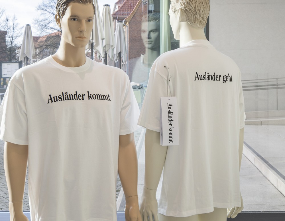 Zwei Schaufensterpuppen tragen weiße T-Shirts mit den Aufschriften „Ausländer kommt" und „Ausländer geht"