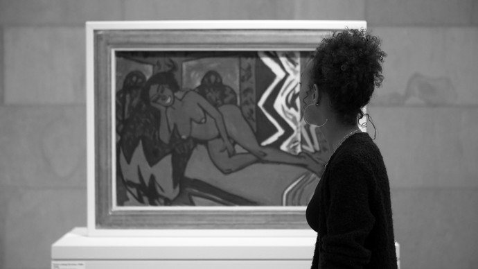 Das Foto zeigt eine Frau, die vor einem gerahmten Kunstwerk steht, das an einer Wand ausgestellt ist.