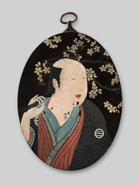 Wandplakette mit kostümierten Kabuki-Schauspieler auf schwarzem Grund.
