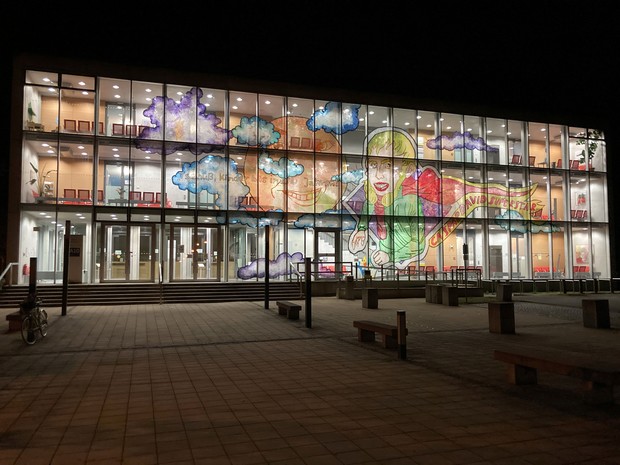 Eine Aufnahme eines Glasgebäudes bei Nacht, auf den Fenstern ist eine künstlerische Bemalung zu sehen.