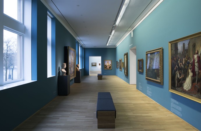 Das Foto zeigt einen Blick in einen Ausstellungsraum mit Gemälden an den Wänden.