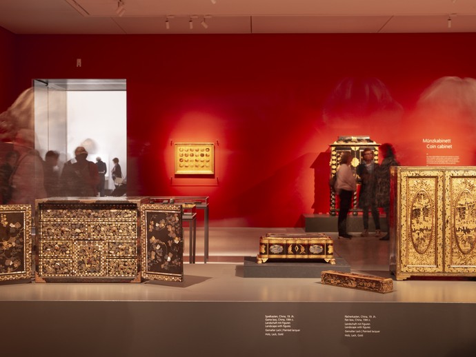 Das Bild zeigt eine Aufnahme aus der Ausstellung. Zu sehen ist ein roter Raum mit zwei Lack-Objekt, die aussehen wie kleine Schränkchen. (vergrößerte Bildansicht wird geöffnet)