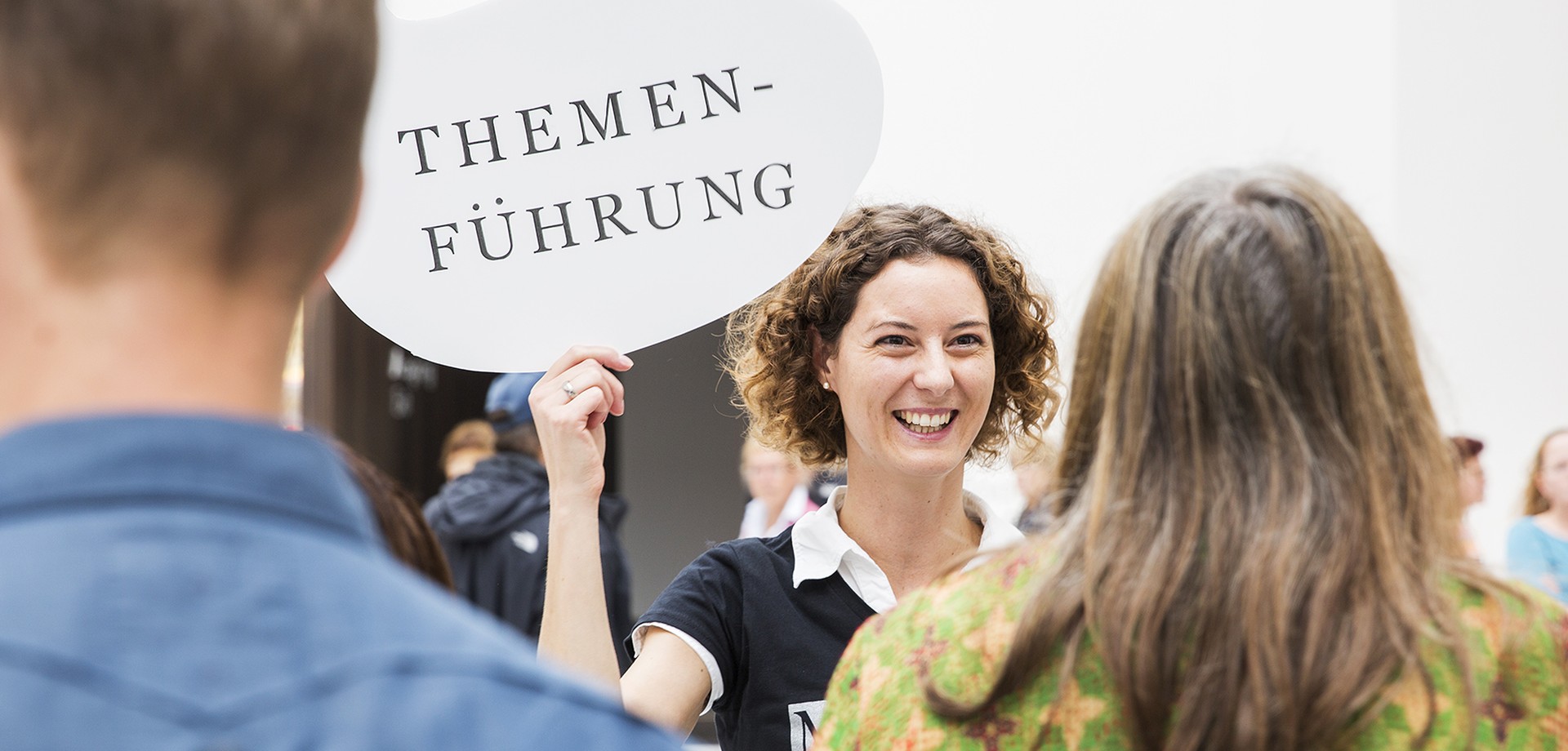 Eine Frau hält ein Schild hoch auf dem "Themenführung" steht.